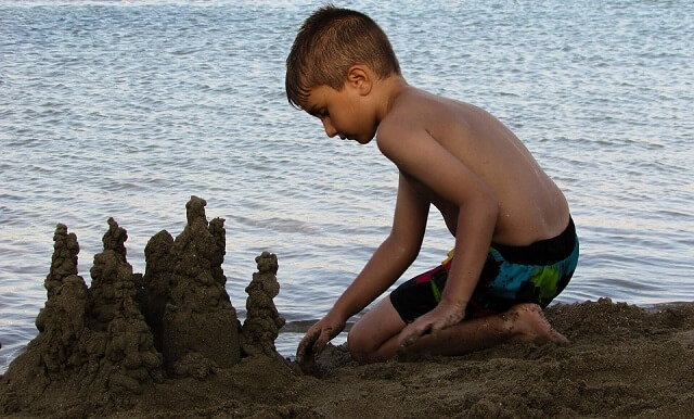 Criança fazendo castelo de areia na praia (Foto: Banco de Imagens Pixabay)